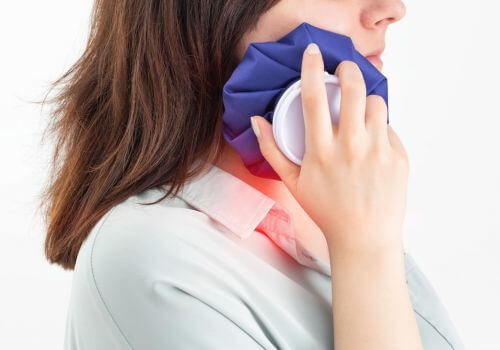 Woman holding ice pack to her jaw after wisdom tooth extraction surgery