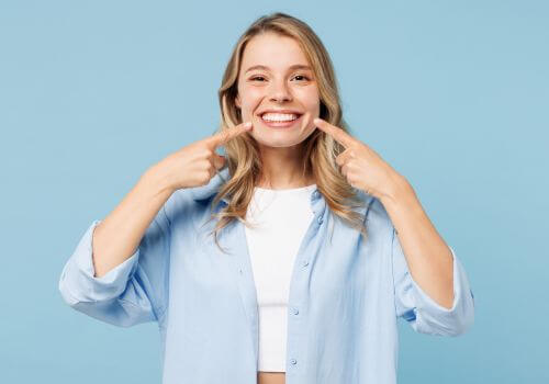 Young woman using both hands to point at her bright, white smile