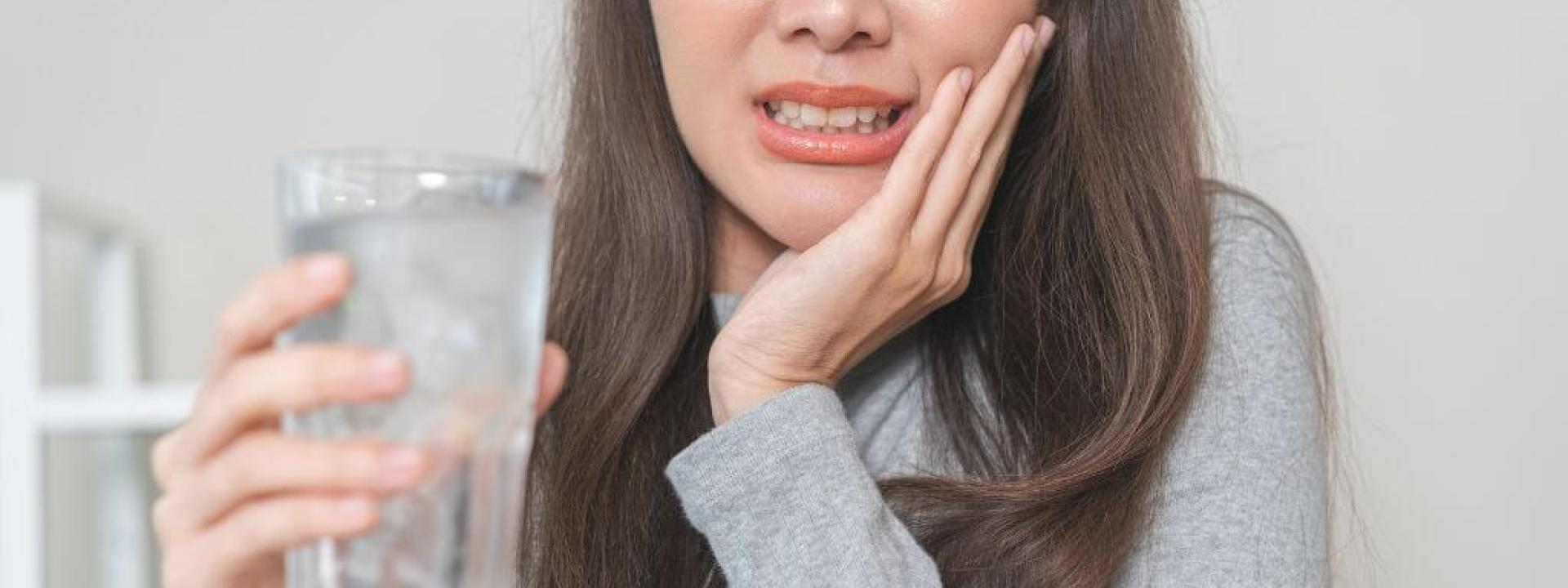 Woman with sensitive teeth, holding glass of ice water